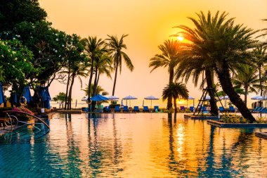 Şemsiye sandalyeli güzel palmiye ağacı gündoğumunda lüks otel tatil beldesinde - tatil ve tatil konsepti