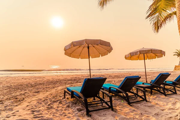 Güneş doğarken palmiye ağacı ve deniz plajı olan şemsiye koltuğu plajı - tatil ve tatil konsepti