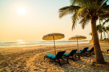 Güneş doğarken palmiye ağacı ve deniz plajı olan şemsiye koltuğu plajı - tatil ve tatil konsepti