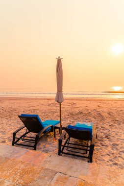 Güneş doğarken palmiye ağacı ve deniz plajı olan şemsiye koltuğu plajı - tatil ve tatil konsepti