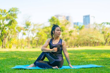 Asyalı kadın yoga yapıyor ve yazın yeşil parkta spor kıyafetleriyle rahatlıyor.