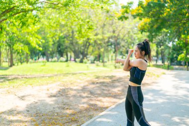 Parkta egzersiz yapmadan önce esneme hareketleri yapan Asyalı kadın.