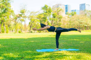 Asyalı kadın yoga yapıyor ve yazın yeşil parkta spor kıyafetleriyle rahatlıyor.