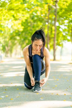 Asyalı kadın ayakkabı bağcıklarını bağlıyor ve parkta koşuya hazırlanıyor.