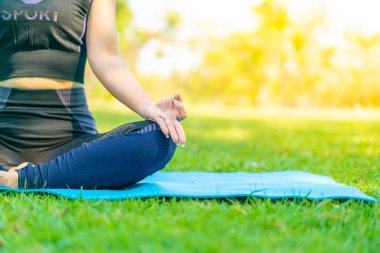 Asyalı kadın yoga yapıyor ve yazın yeşil parkta spor kıyafetleriyle rahatlıyor.