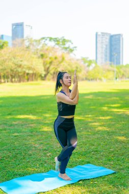 Asyalı kadın yoga yapıyor ve yazın yeşil parkta spor kıyafetleriyle rahatlıyor.