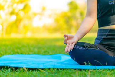 Asyalı kadın yoga yapıyor ve yazın yeşil parkta spor kıyafetleriyle rahatlıyor.