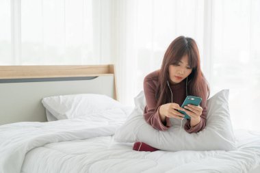 Güzel Asyalı kadınlar yatakta akıllı telefon oynuyorlar.