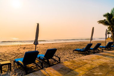 Güneş doğarken palmiye ağacı ve deniz plajı olan şemsiye koltuğu plajı - tatil ve tatil konsepti