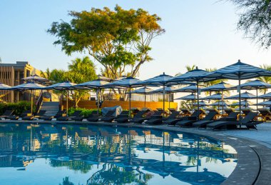 Seyahat tatili konsepti için otel tatil beldesinde yüzme havuzunun etrafında şemsiye ve sandalye.