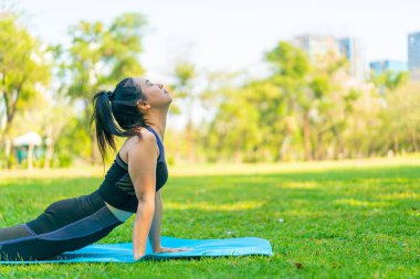 Asyalı kadın yoga yapıyor ve yazın yeşil parkta spor kıyafetleriyle rahatlıyor.