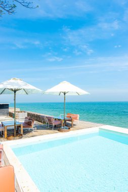 Yüzme havuzu ve tatil konsepti için deniz sahili geçmişi olan güzel, boş sandalye ve şemsiye.