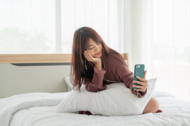 Güzel Asyalı kadınlar yatakta akıllı telefon oynuyorlar.