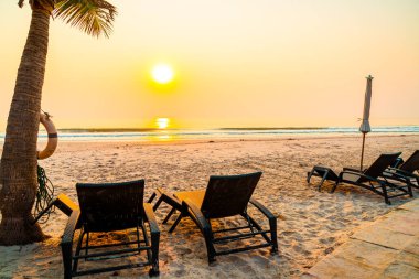 Güneş doğarken palmiye ağacı ve deniz plajı olan şemsiye koltuğu plajı - tatil ve tatil konsepti