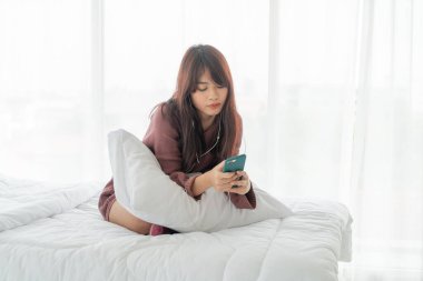 Güzel Asyalı kadınlar yatakta akıllı telefon oynuyorlar.