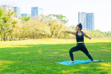 Asyalı kadın yoga yapıyor ve yazın yeşil parkta spor kıyafetleriyle rahatlıyor.