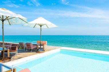 Yüzme havuzu ve tatil konsepti için deniz sahili geçmişi olan güzel, boş sandalye ve şemsiye.