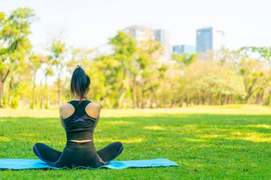 Asyalı kadın yoga yapıyor ve yazın yeşil parkta spor kıyafetleriyle rahatlıyor.