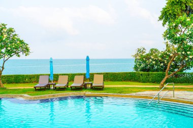 Sandalye havuzu ve şemsiyeyle okyanus arka planında yüzme havuzu
