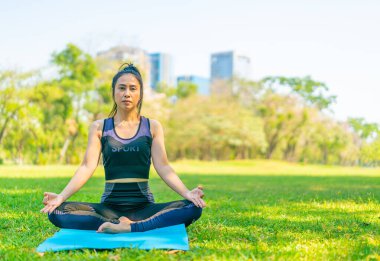 Asyalı kadın yoga yapıyor ve yazın yeşil parkta spor kıyafetleriyle rahatlıyor.