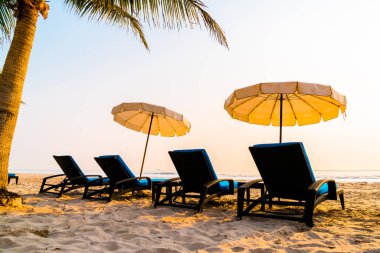 Güneş doğarken palmiye ağacı ve deniz plajı olan şemsiye koltuğu plajı - tatil ve tatil konsepti