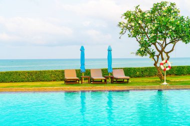 Sandalye havuzu ve şemsiyeyle okyanus arka planında yüzme havuzu
