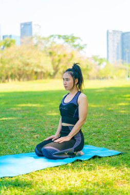 Asyalı kadın yoga yapıyor ve yazın yeşil parkta spor kıyafetleriyle rahatlıyor.