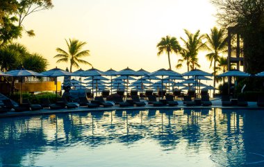 Seyahat tatili konsepti için otel otelinde yüzme havuzunun etrafında şemsiye ve havuz yatağı.