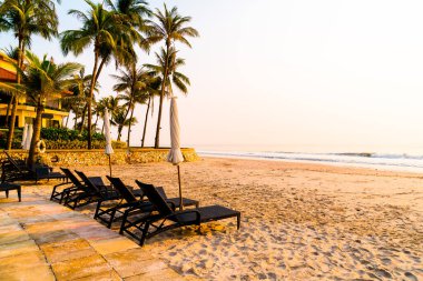 Güneş doğarken palmiye ağacı ve deniz plajı olan şemsiye koltuğu plajı - tatil ve tatil konsepti