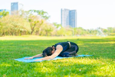 Asyalı kadın yoga yapıyor ve yazın yeşil parkta spor kıyafetleriyle rahatlıyor.