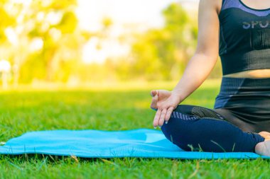 Asyalı kadın yoga yapıyor ve yazın yeşil parkta spor kıyafetleriyle rahatlıyor.
