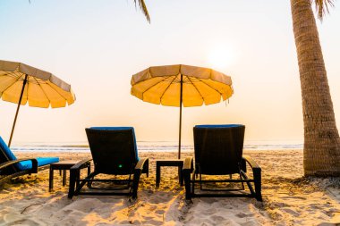 Güneş doğarken palmiye ağacı ve deniz plajı olan şemsiye koltuğu plajı - tatil ve tatil konsepti