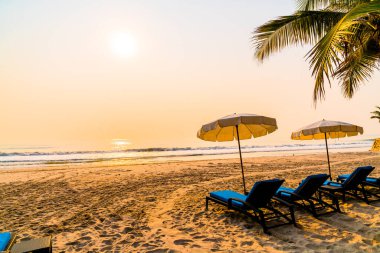 Güneş doğarken palmiye ağacı ve deniz plajı olan şemsiye koltuğu plajı - tatil ve tatil konsepti