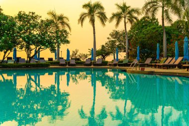 Gün batımında yüzme havuzunda şemsiyeli plaj sandalyesi ya da bilardo yatağı