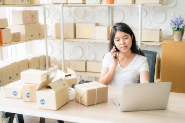 Asyalı bir kadın internette dizüstü bilgisayar ve ofis telefonlarını kullanırken eğleniyor - online veya çevrimiçi alışveriş kavramı satmak