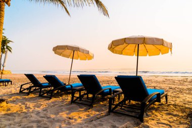 Güneş doğarken palmiye ağacı ve deniz plajı olan şemsiye koltuğu plajı - tatil ve tatil konsepti