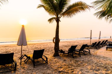 Güneş doğarken palmiye ağacı ve deniz plajı olan şemsiye koltuğu plajı - tatil ve tatil konsepti
