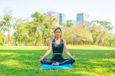 Asyalı kadın yoga yapıyor ve yazın yeşil parkta spor kıyafetleriyle rahatlıyor.