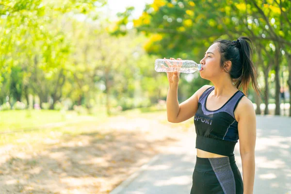 Asian woman drinking water in sportwear after exercise at park