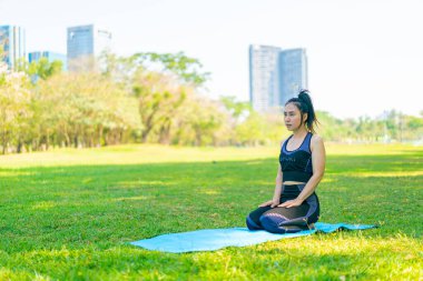 Asyalı kadın yoga yapıyor ve yazın yeşil parkta spor kıyafetleriyle rahatlıyor.