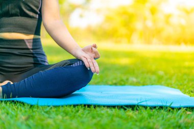 Asyalı kadın yoga yapıyor ve yazın yeşil parkta spor kıyafetleriyle rahatlıyor.