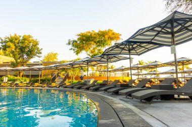 Seyahat tatili konsepti için otel otelinde yüzme havuzunun etrafında şemsiye ve havuz yatağı.