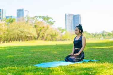 Asyalı kadın yoga yapıyor ve yazın yeşil parkta spor kıyafetleriyle rahatlıyor.