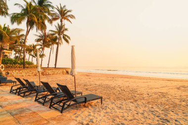 Güneş doğarken palmiye ağacı ve deniz plajı olan şemsiye koltuğu plajı - tatil ve tatil konsepti