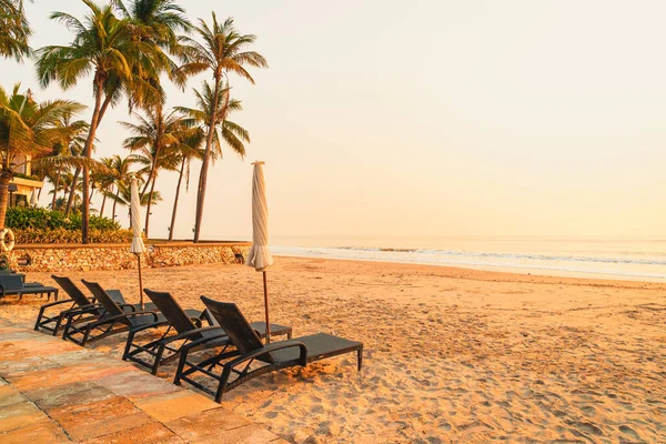 Güneş doğarken palmiye ağacı ve deniz plajı olan şemsiye koltuğu plajı - tatil ve tatil konsepti