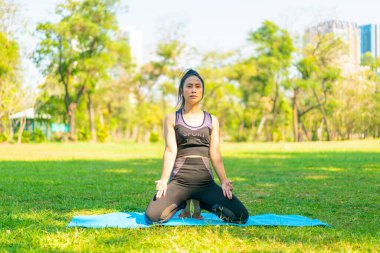 Asyalı kadın yoga yapıyor ve yazın yeşil parkta spor kıyafetleriyle rahatlıyor.