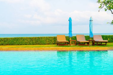 Sandalye havuzu ve şemsiyeyle okyanus arka planında yüzme havuzu