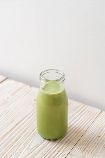 matcha green tea with milk in bottle on wood background