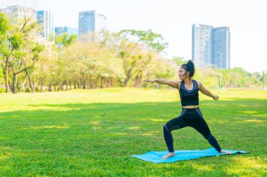 Asyalı kadın yoga yapıyor ve yazın yeşil parkta spor kıyafetleriyle rahatlıyor.