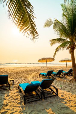 Güneş doğarken palmiye ağacı ve deniz plajı olan şemsiye koltuğu plajı - tatil ve tatil konsepti